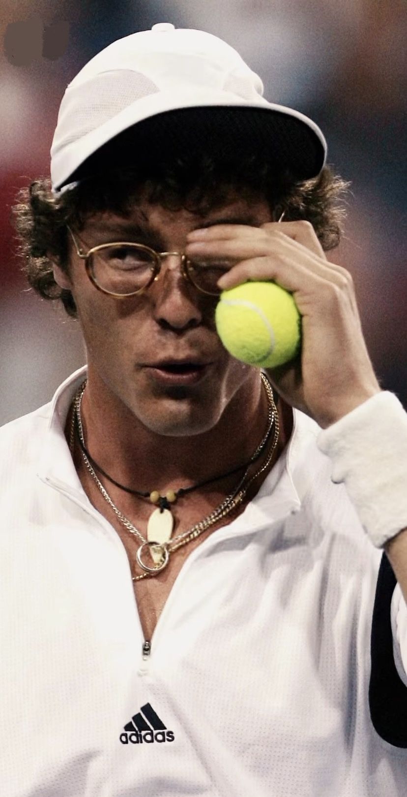 Player holding a tennis ball to their eye behind round glasses